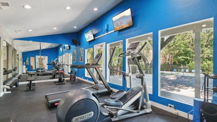 a gym room with blue walls and tread machines at The Cross Creek Apartments